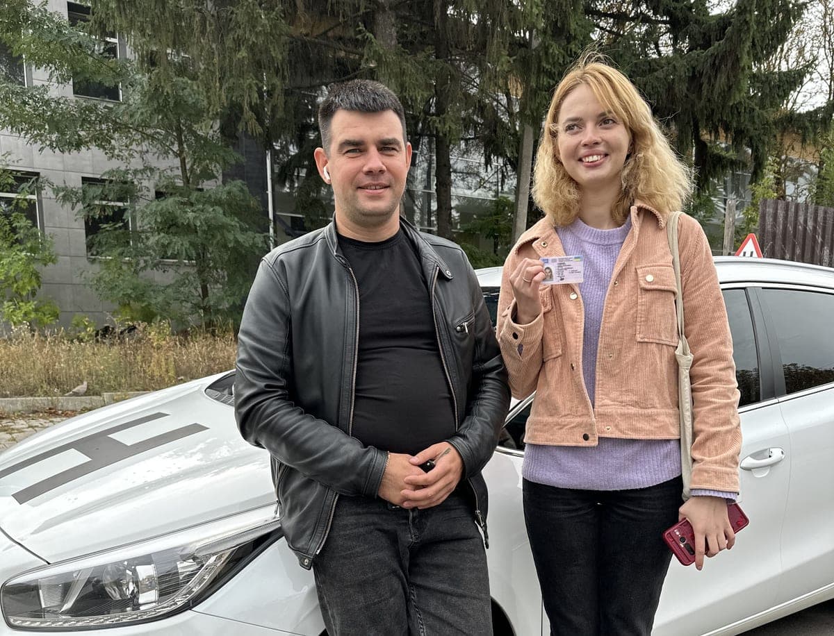 Інструктор і випускниця з посвідченням водія біля навчального авто автошколи Лідер